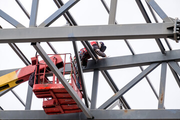 Man welder working on a crane performs high-rise work on welding metal structures of tower at a height.