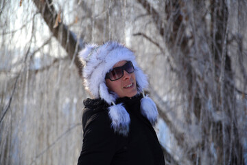 Fototapeta na wymiar Beautiful young woman smiling in an interesting winter hat in front of frozen tree