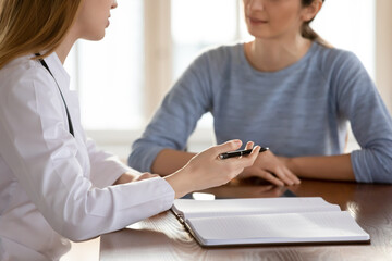 Crop close up of female doctor in white medical uniform consult patient at private meeting in hospital. Woman GP or physician talk speak with client at consultation, make notes in journal in clinic.