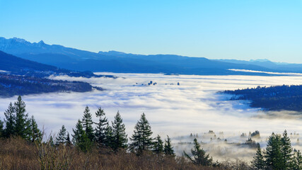 High-rise  buildings peeking through dense cloud cover over valley surrounded by alpine mountains