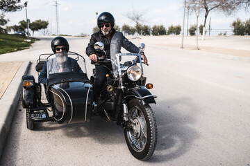 Mature man poses in front of his sidecar with strap and leather jacket with the motorcycle parked