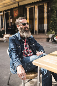 Bearded man smokes a cigar sitting on the terrace of a bar