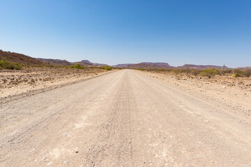 Gravel road crossing the Namib desert, in the majestic Namib Naukluft National Park, best travel destination in Namibia, Africa. Toned image, vintage old retro filter.