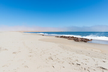 Sandy beach and coast line on the Atlantic ocean at Cape Cross, Namibia, famous for the nearby seal colony. Clear blue sky.