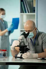 Mature bald scientist in protective mask and gloves studying chemical samples