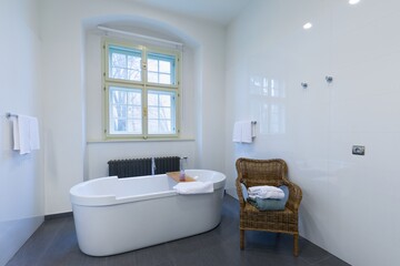 Fototapeta na wymiar Comfortable white bathtub and sink standing in modern bathroom with white walls and concrete floor. Interior with spectacular oval bath. 