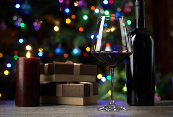 Glass of red wine on table with gift boxes. Christmas lights in the background.