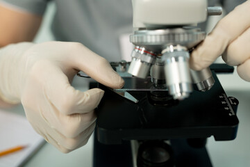 Gloved hand of scientist or clinician putting glass with chemical sample by lens