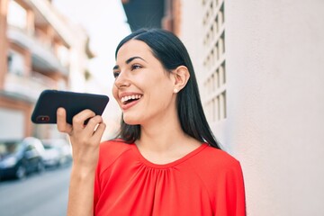 Young latin girl smiling happy sending voice message using smartphone at the city.