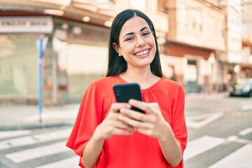 Young latin girl smiling happy using smartphone at the city.