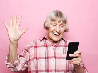 old grandmother is talking to her grandchildren by phone, smiling and greeting them.