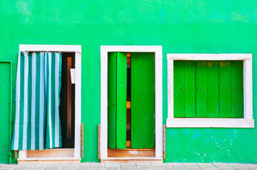 Green painted facade of the house and door and windows with green shutters. Colorful architecture in Burano island, Venice, Italy.