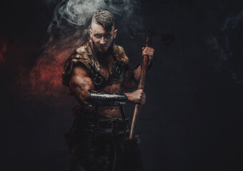 Assaulting savage viking armed with two handed axe and looking at camera in dark background.