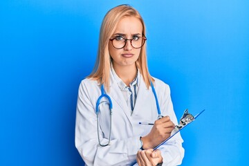 Beautiful caucasian blonde woman wearing doctor stethoscope holding clipboard skeptic and nervous,...
