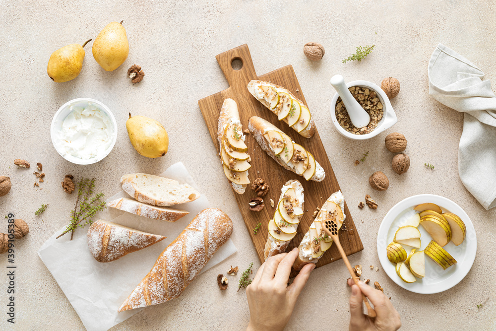 Wall mural Woman's hands cooking sweet open sandwiches with ricotta cheese, fresh pears, walnuts and honey on kitchen table for family breakfast, overhead view