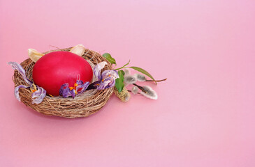 Easter composition, red egg, symbol of faith, in a basket shaped like a nest on a pink background, space for text