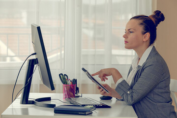 Side view profile of thoughtful young woman sitting near laptop and holding a notebook.