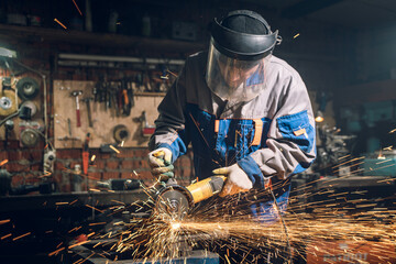 Locksmith in special clothes and goggles works in production. Metal processing with angle grinder....