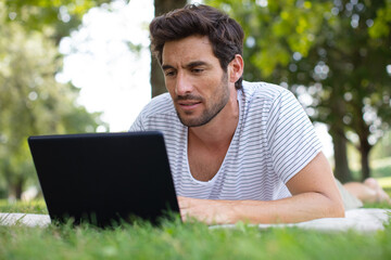 man lying down on the grass typing on his laptop