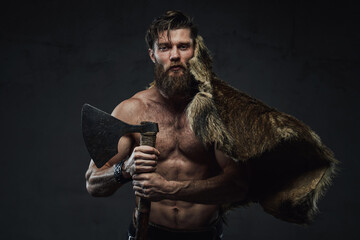 Medieval scandinavian warrior with muscular naked build posing with his hunting trophy and axe in...
