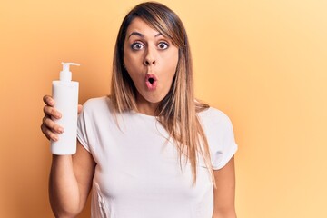 Young beautiful woman holding bottle of cream lotion scared and amazed with open mouth for surprise, disbelief face