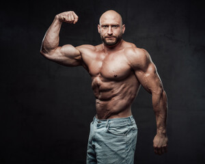 Fototapeta na wymiar Bearded and hairless man with powerful and muscular build in jeans shorts poses with serious face in dark background looking at camera.