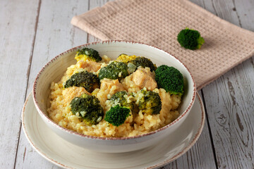 Creamy risotto with chicken and broccoli on wooden background