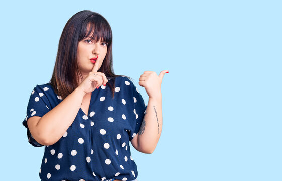 Young plus size woman wearing casual clothes asking to be quiet with finger on lips pointing with hand to the side. silence and secret concept.