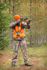 adult hunter aiming deer rifle in forest