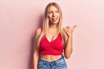 Young blonde woman wearing casual clothes pointing thumb up to the side smiling happy with open...