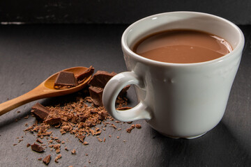 Chocolate milk drink presented with a wooden spoon and crumbled chocolate on the side.