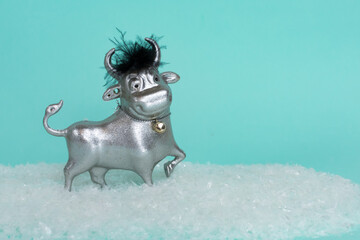 A toy bull on a blue background stands in the snow. The symbol of the new 2021. Good New Year mood....