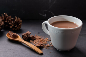 Chocolate milk drink presented with a wooden spoon and crumbled chocolate on the side nd decorated with pinecones.