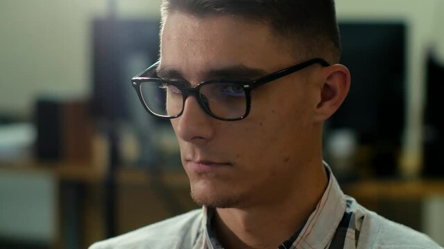 Close-up video portrait of a young man wearing glasses working at the computer at his workplace in the office.