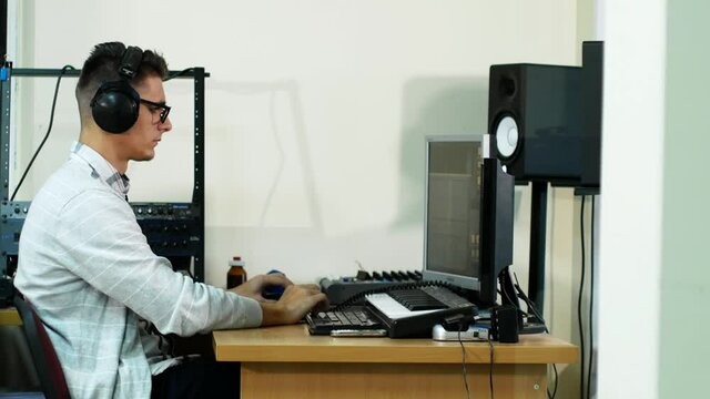 young man in glasses and headphones working at the computer at his workplace in the office. The sound engineer of the TV channel against the background of the sound equipment control