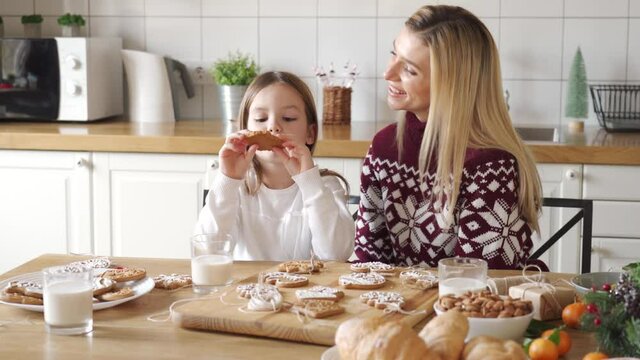 Happy dad wearing santa hat giving excited cute small kid daughter xmas gift sitting at kitchen table. Family parents preparing present for child girl hugging celebrating Christmas holiday at home.