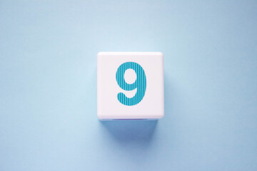 Close-up photo of a white plastic cube with a blue number 9 on a blue background. Object in the...