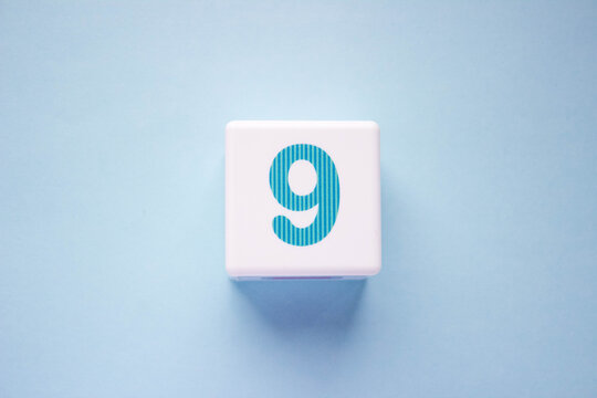 Close-up photo of a white plastic cube with a blue number 9 on a blue background. Object in the center of the photo