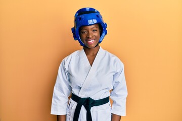 Young african american girl wearing taekwondo kimono and protection helmet with a happy and cool smile on face. lucky person.