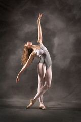 Young adult ballerina in the studio, dancing in gray leotard.
