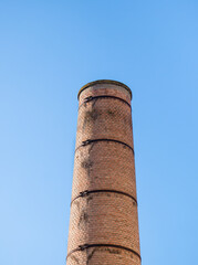 Old factory chimney made of red bricks against blue sky.