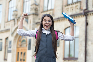 Happy kid show power hand gesture holding school book outdoors, knowledge