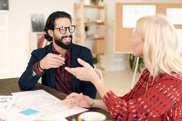 Young smiling businessman and his blond mature colleague discussing new ideas