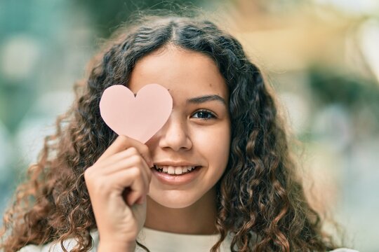 Hispanic teenager girl smiling happy holding heart over eye at the city.