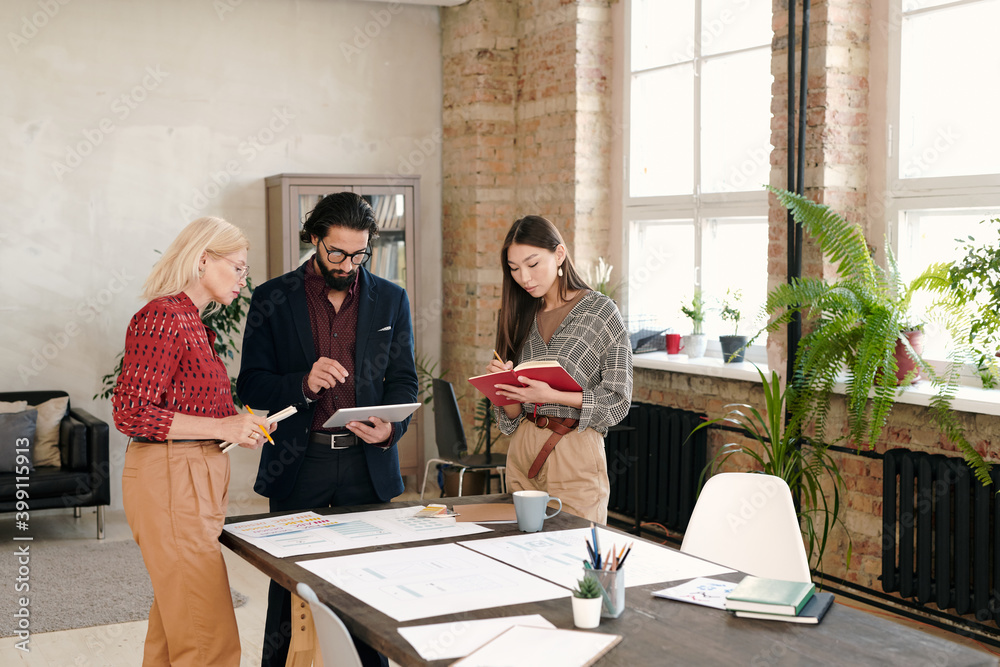 Poster Two elegant females making notes and looking at display of tablet held by man