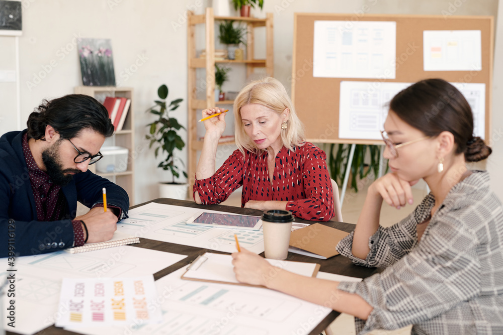 Poster Creative designers brainstorming while working individually by table in office