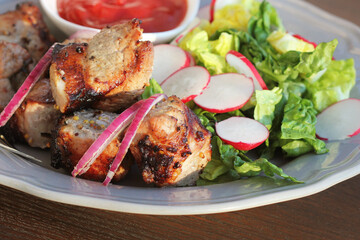 Grilled meat kebab and healthy vegetable salad of fresh radish, onion, lettuce on brown background