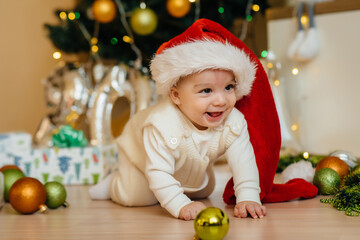 Fototapeta na wymiar Cute smiling baby is lying under a festive Christmas tree and playing with gifts. Christmas and New Year celebrations