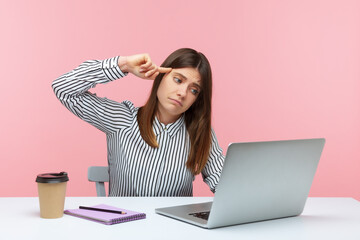 Depressed unhappy woman office worker in striped shirt sitting workplace showing stupid gesture to...