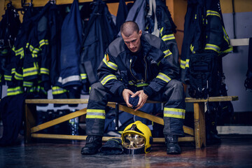 Young attractive fireman in protective uniform sitting in fire station and waiting for other firemen. He is prepared for action.